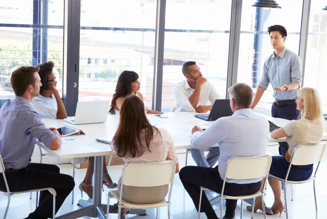 A diverse group of individuals engaged in discussion around a conference table in a meeting room.